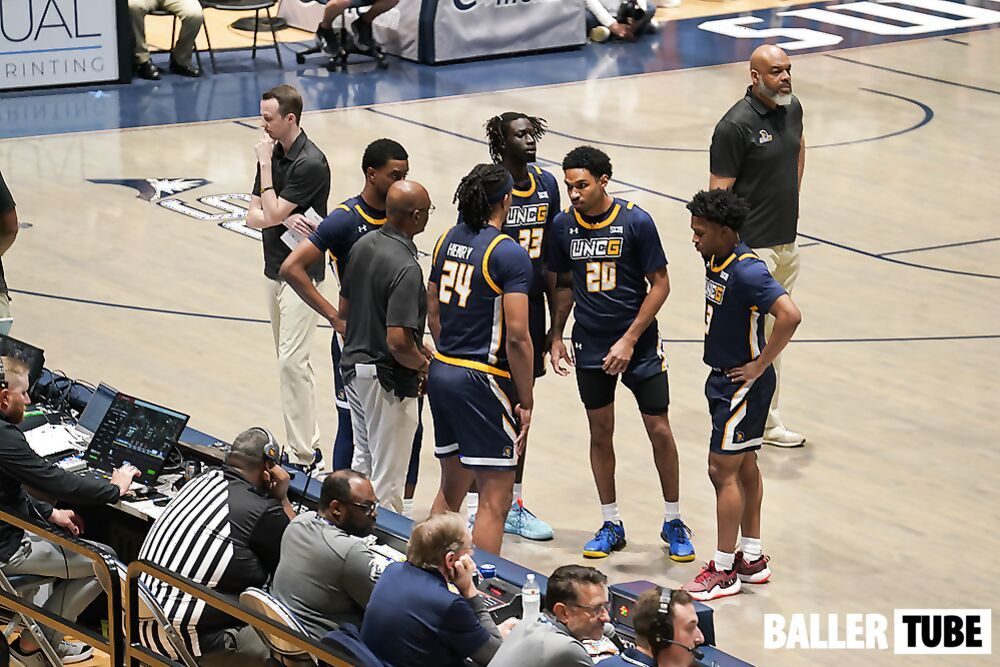 Coaches and players in a timeout huddle being filmed courtside